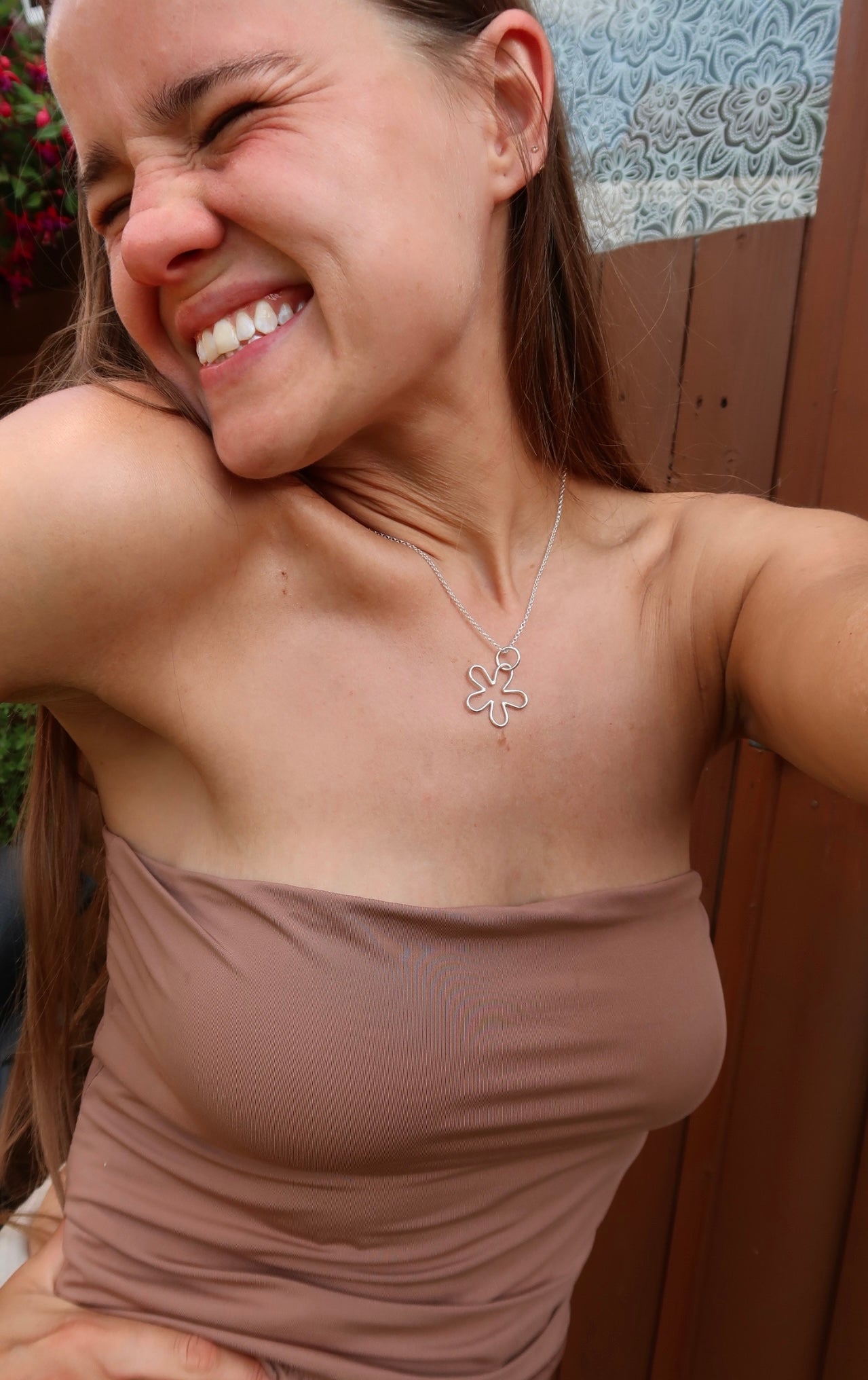Close-up of a tanned woman wearing a handmade sterling silver nature and beach inspired necklace pendant small flower pendant. She is wearing bohemian style clothes and fashion