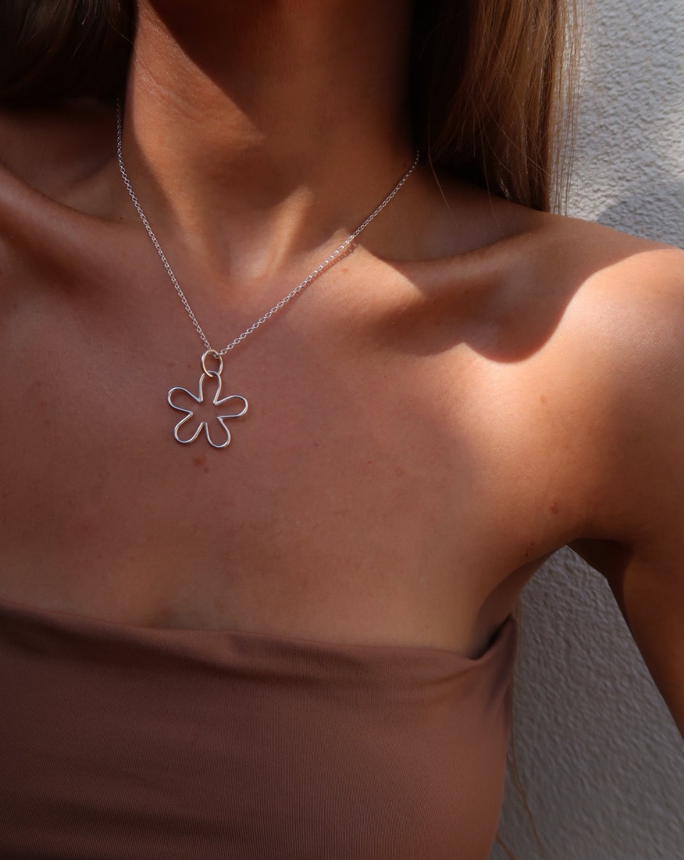 Close-up of a tanned woman wearing a handmade sterling silver nature and beach inspired necklace pendant small flower pendant. She is wearing bohemian style clothes and fashion