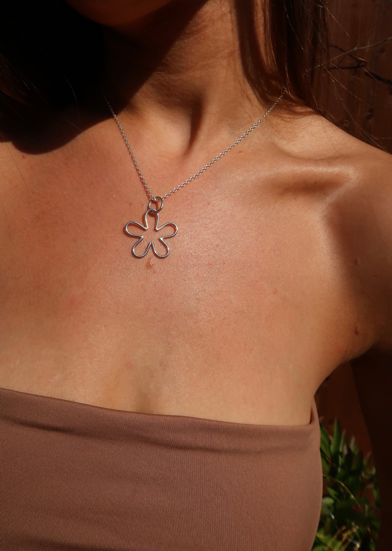 Close-up of a tanned woman wearing a handmade sterling silver nature and beach inspired necklace pendant small flower pendant. She is wearing bohemian style clothes and fashion brown banedu top