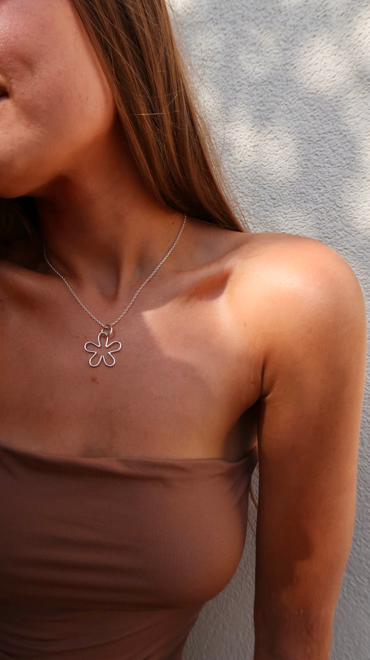 Close-up of a tanned woman wearing a handmade sterling silver nature and beach inspired necklace pendant small flower pendant. She is wearing bohemian style clothes and fashion