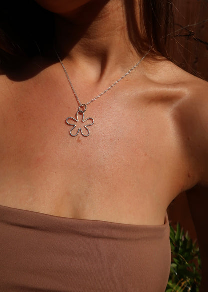 Close-up of a tanned woman wearing a handmade sterling silver nature and beach inspired necklace pendant small flower pendant. She is wearing bohemian style clothes and fashion brown banedu top